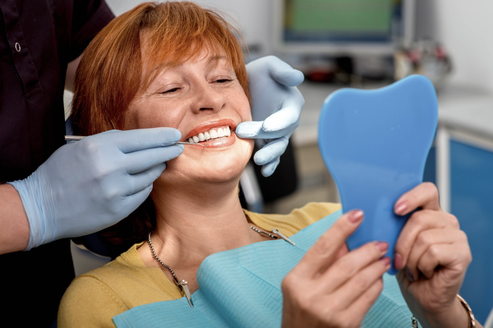 woman smiling into a mirror after getting dentures in apex