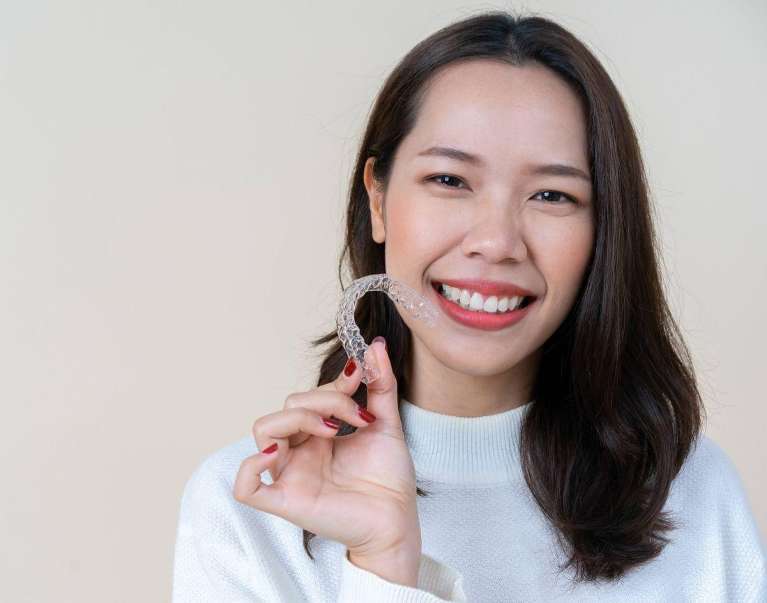 A woman smiling while holding a clear aligner in Apex, NC